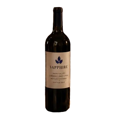 A full shot of a dark glass wine bottle isolated on a clean white background. The bottle features a light beige label reading "SAPPHIRE NAPA VALLEY CABERNET SAUVIGNON ADAGIO VINEYARD VINTAGE 2022" beneath a distinct blue three-leaf or droplet logo emblem.