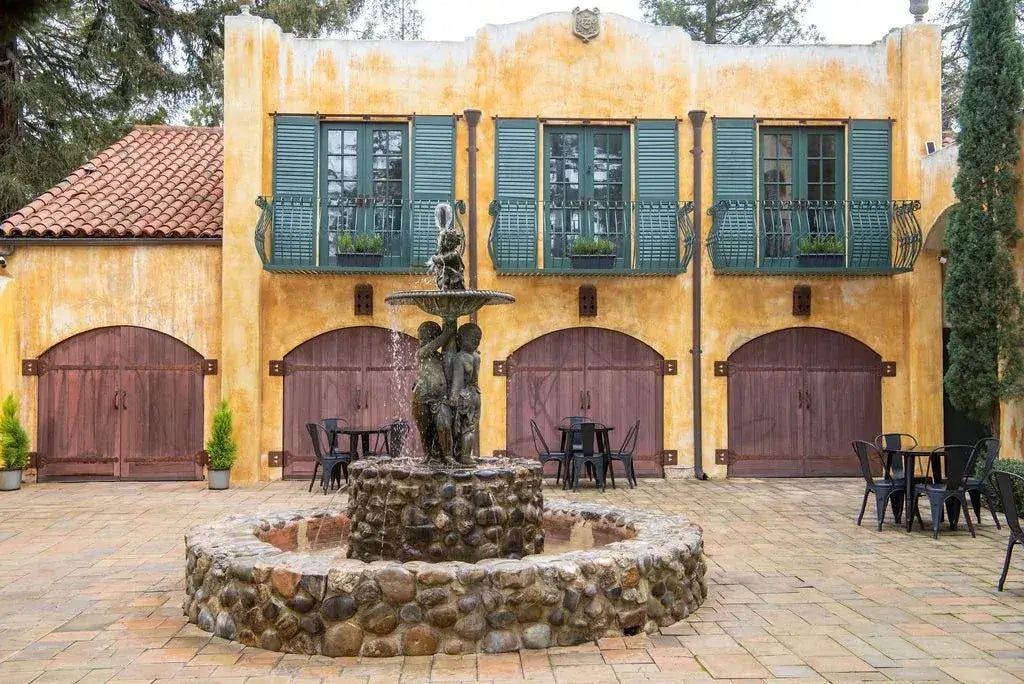 Yellow winery with green shutters featuring a stone fountain in front.